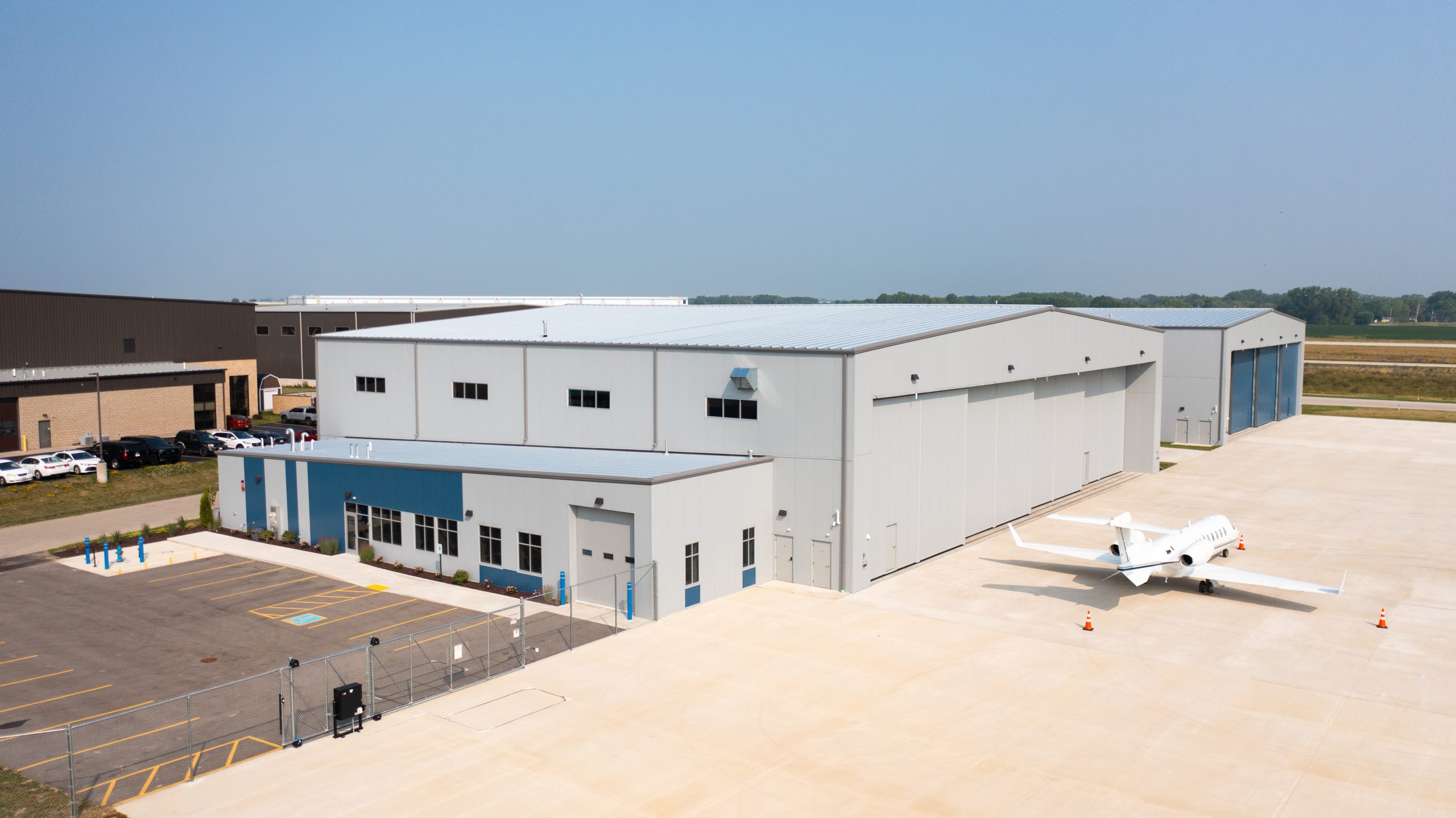 Aerial view of a modern aircraft hangar complex with a small jet parked on an asphalt tarmac, showcasing a spacious, well-maintained facility designed for aviation services.