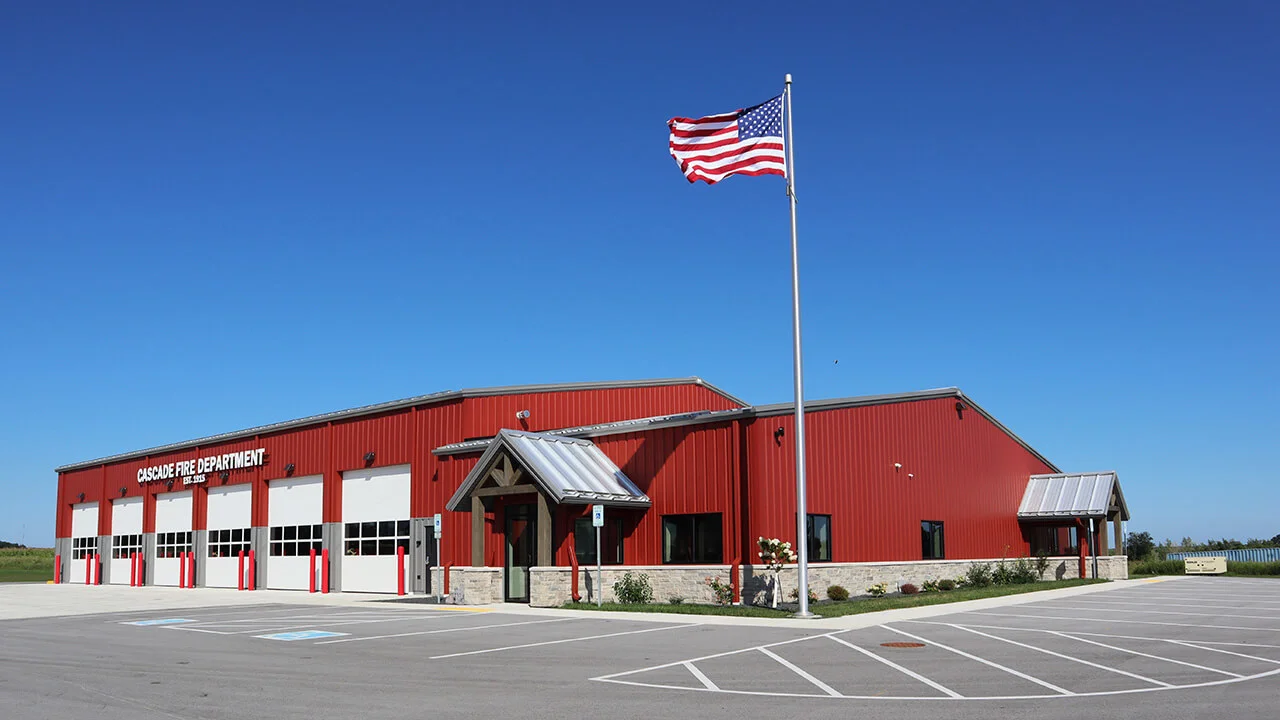 Modern Cascade Fire Department building with red exterior, American flag flying, and multiple garage doors visible under a clear blue sky.