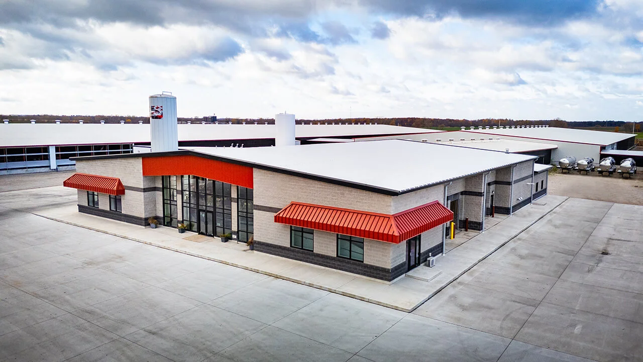 Modern industrial building with a red accent roof, large glass windows, and a spacious parking area, designed for commercial use. The structure features a centrally located tower, surrounded by additional industrial facilities and equipment.