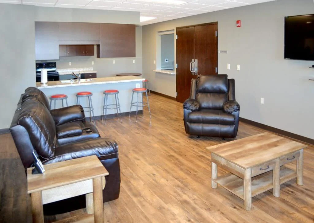 Modern living room featuring comfortable black leather furniture, a wooden coffee table, and a well-equipped kitchen area with bar stools and sleek cabinetry. Ideal for entertaining or relaxing, the space showcases hardwood flooring and neutral wall colors.