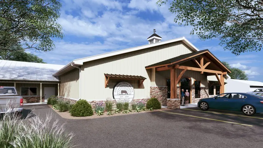 Exterior view of Country Pride Meats, showcasing its welcoming entrance with a wooden canopy and stone accents, surrounded by landscaped greenery, parked vehicles, and a clear blue sky. The establishment, founded in 2009, emphasizes quality meat products and customer service.