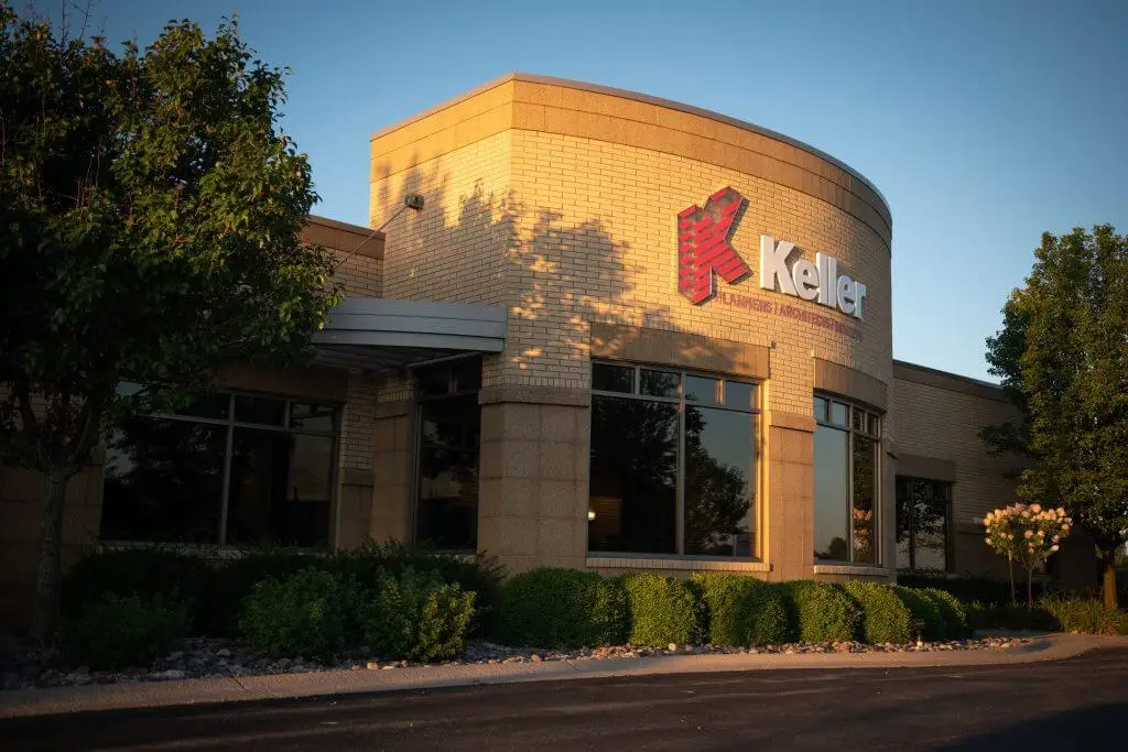 Exterior view of the Keller building, showcasing a modern architectural design with large windows and neatly landscaped surroundings in the golden light of sunset. The prominent Keller logo is displayed on the facade, indicating the company's presence in the area.