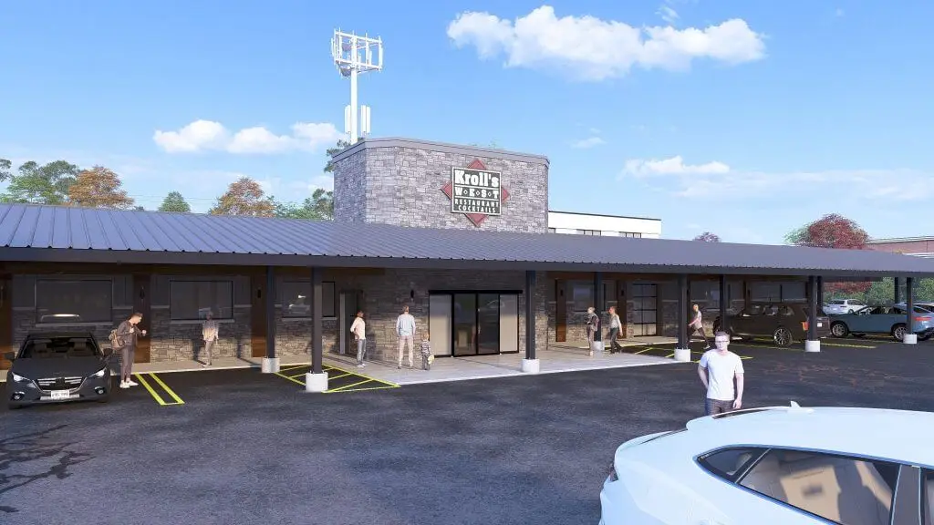 Exterior view of Kroll's Restaurant featuring a modern design with stone facade, outdoor seating area, and parking lot. Customers are arriving and leaving, showcasing a welcoming atmosphere and accessibility.