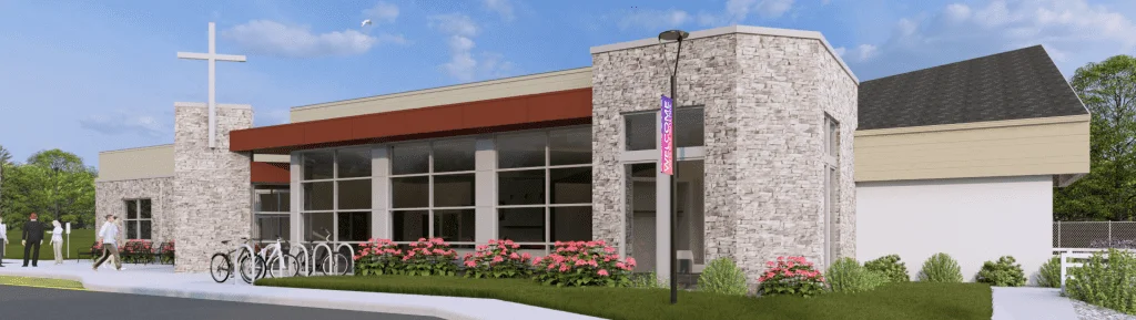 Exterior view of a modern church building featuring a prominent cross, large glass windows, and landscaped flower beds. The entrance includes a welcome sign and bike racks, with people walking in the vicinity, set against a clear blue sky and green trees.